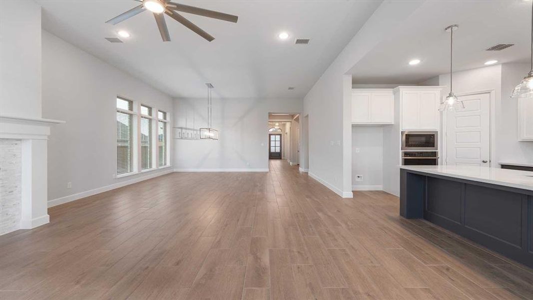 Unfurnished living room featuring a stone fireplace, ceiling fan, and light wood-type flooring