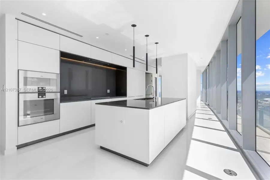 Modern kitchen featuring flat-panel cabinetry, a central island with a solid surface countertop, built-in stainless steel appliances, floor-to-ceiling windows, and matte black pendant lighting