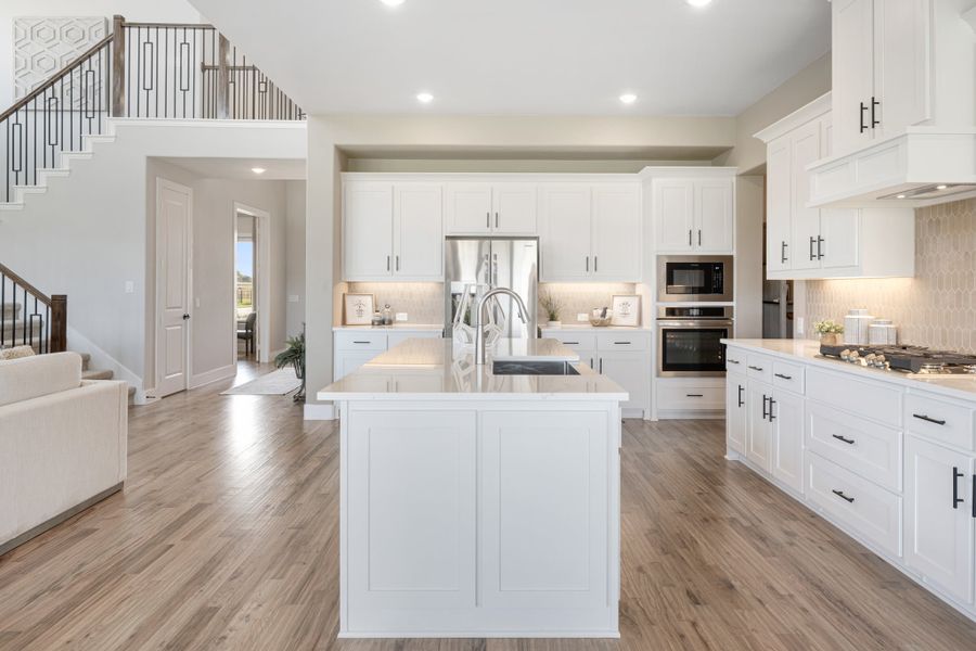 Open kitchen with white cabinets, center island, stainless appliances, and wood floors, open to staircase and living area