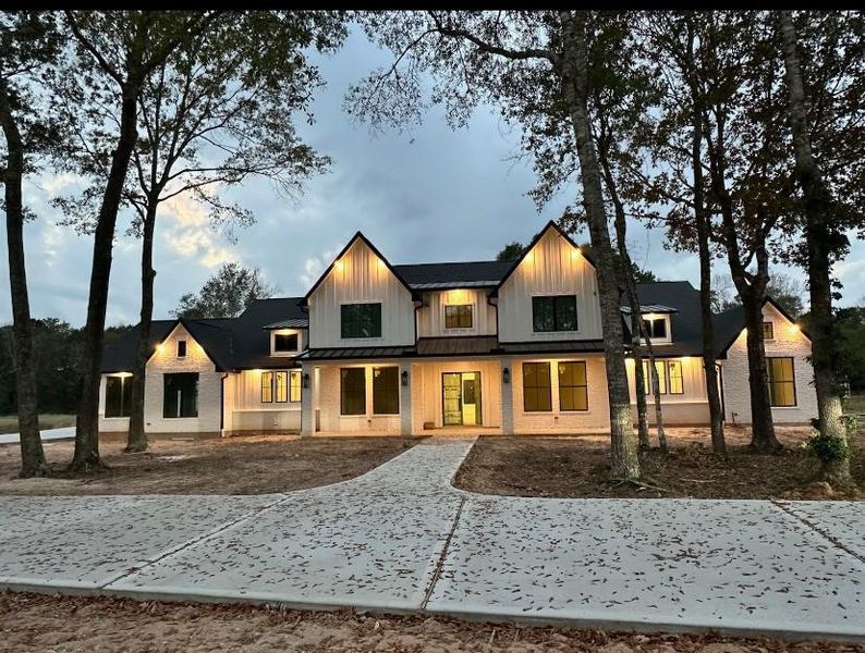 Striking dusk time view of this estate at 18332 Woodstream Crossing, beautifully illuminated among the trees—showcasing the grandeur of the main residence and adjoining 438 sqft casita with dramatic architectural lighting. This over 4000 sqft home has everything!
