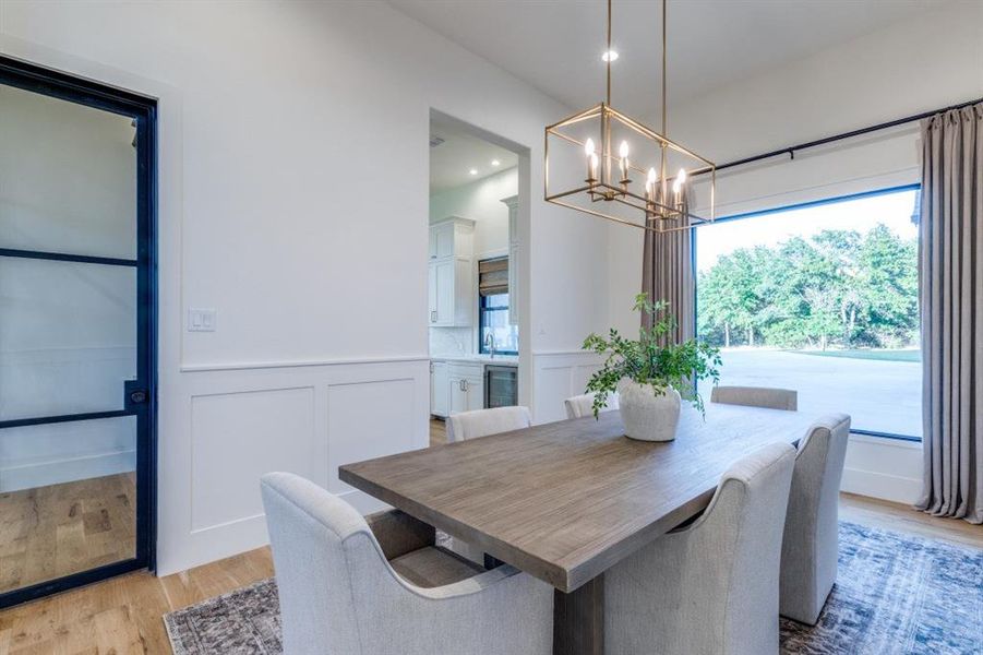 Dining area featuring a decorative wall, wainscoting, light wood-type flooring, and a chandelier Dining area featuring a decorative wall, wainscoting, light wood-type flooring, and a chandelier