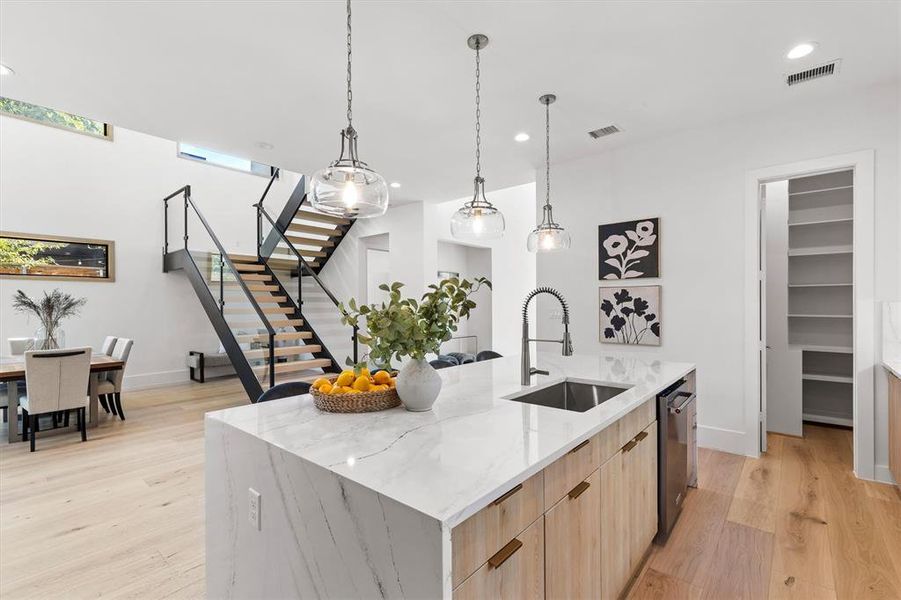 Kitchen featuring sink, stainless steel dishwasher, a large island, light hardwood / wood-style flooring, and light stone countertops