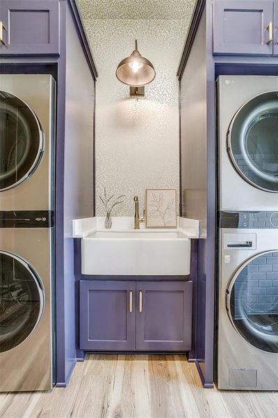 Laundry room featuring stacked washer / drying machine, wallpapered walls, and light wood-style flooring