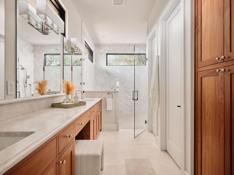 A well-appointed primary bathroom showcases dual vanities with marble countertops, custom cabinetry, and a spacious glass-enclosed shower. A well-appointed primary bathroom showcases dual vanities with marble countertops, custom cabinetry, and a spacious glass-enclosed shower.