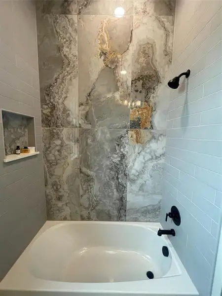 Soaking tub featuring black fixtures and a tiled surround