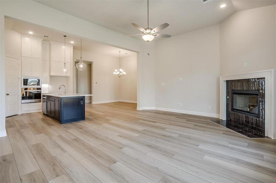 Kitchen with pendant lighting, stainless steel oven, white cabinets, a center island with sink, and light wood-type flooring