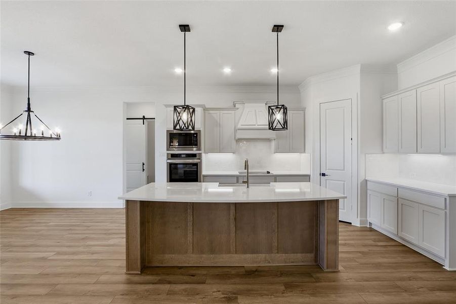 Dual tone kitchen featuring a barn door, two tone cabinets, decorative light fixtures, an island with sink, and decorative backsplash
