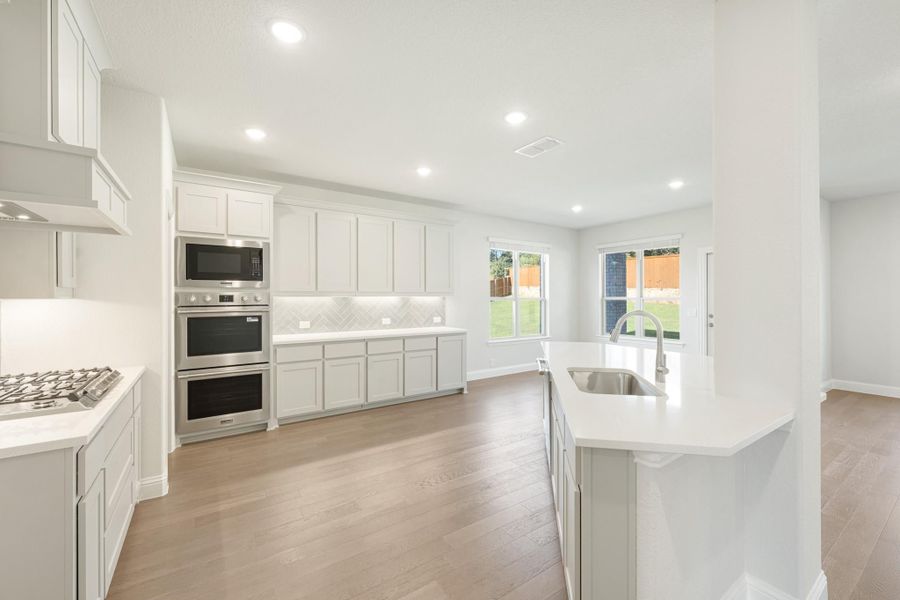 Open kitchen with white cabinets, stainless steel appliances, center island with sink, and light hardwood floors