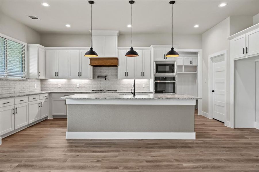Kitchen featuring white cabinets, wood finished floors, stainless steel oven, light stone countertops, and a kitchen island with sink Kitchen featuring white cabinets, wood finished floors, stainless steel oven, light stone countertops, and a kitchen island with sink