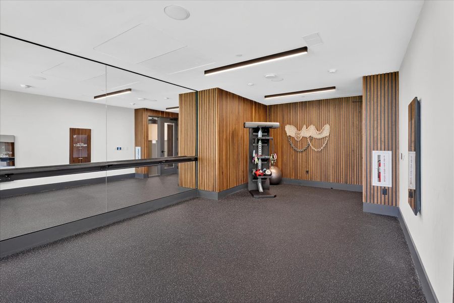 An inviting fitness area boasts resilient flooring, wall-to-wall mirrors, and contemporary lighting, perfect for a workout.