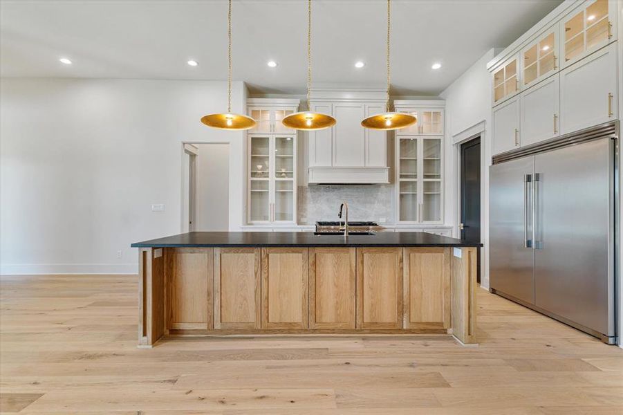 Kitchen featuring stainless steel built in refrigerator, dark countertops, a center island with sink, backsplash, and recessed lighting