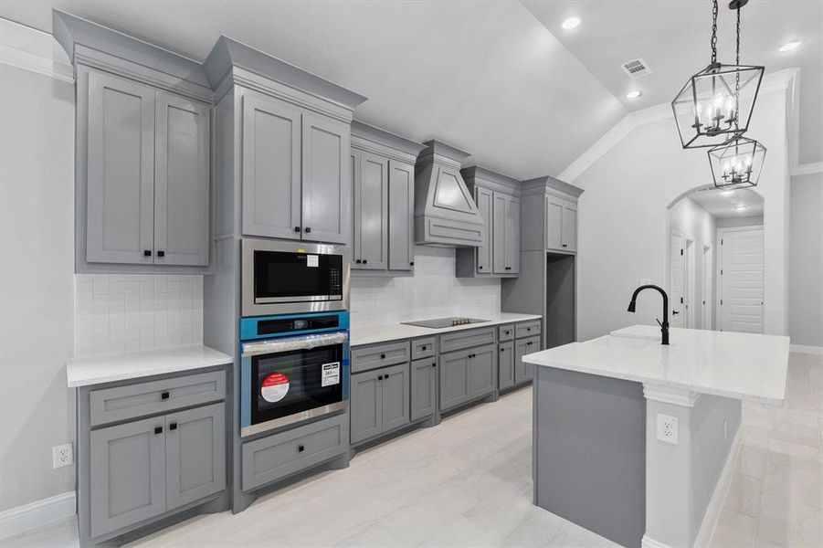 Kitchen featuring decorative backsplash, gray cabinetry, stainless steel appliances, vaulted ceiling, and premium range hood