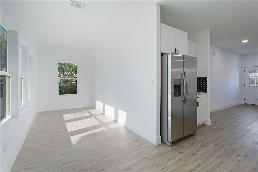 Kitchen with white cabinetry, stainless steel fridge with ice dispenser, a wealth of natural light, and light hardwood / wood-style flooring