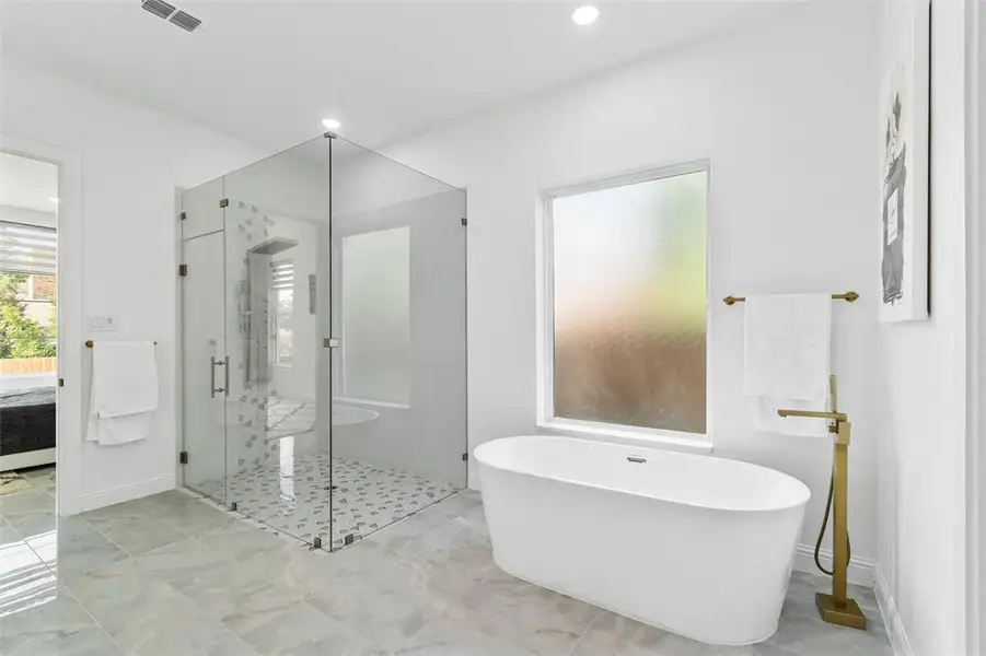 Spacious bathroom featuring a frameless glass shower enclosure with patterned tile, a freestanding soaking tub, and large format floor tiling