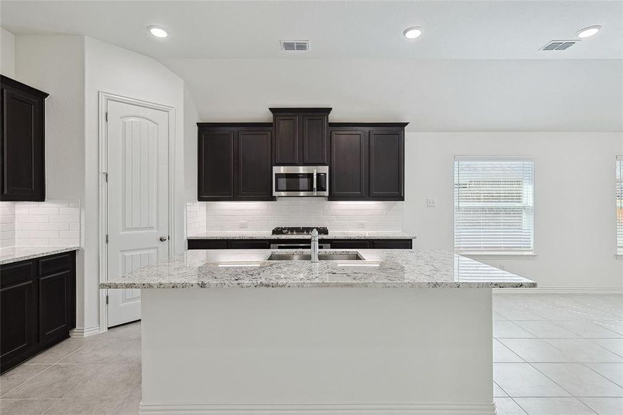 Kitchen with vaulted ceiling, a center island with sink, sink, and decorative backsplash