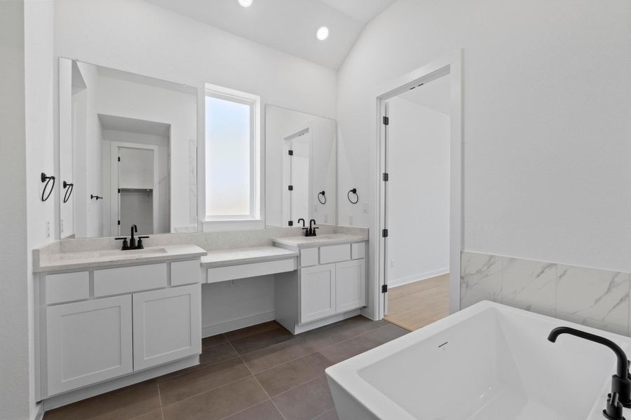 Bathroom with double vanity, a freestanding tub, tile patterned floors, vaulted ceiling, and recessed lighting