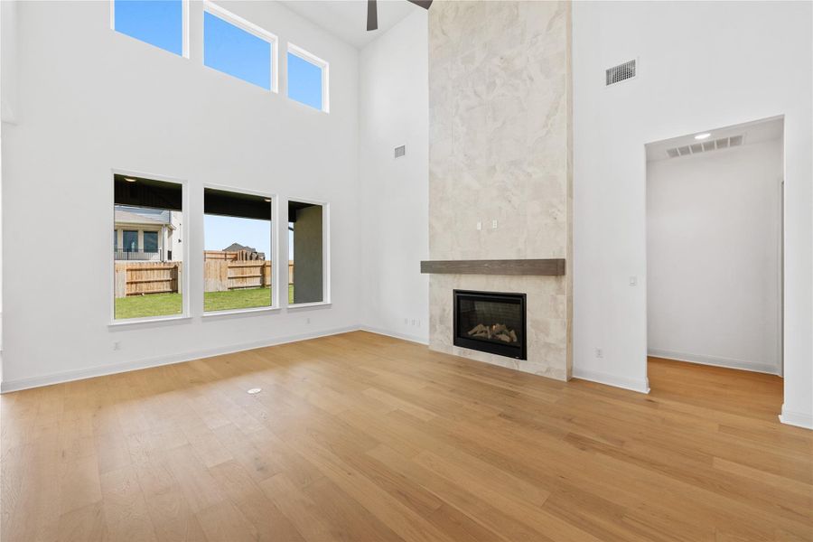 Unfurnished living room with a high ceiling, a tile fireplace, light wood-style flooring, and ceiling fan
