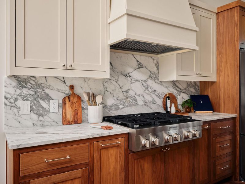 Elegant kitchen features rich wooden cabinetry complemented by sleek marble countertops and a stainless steel gas range. Elegant kitchen features rich wooden cabinetry complemented by sleek marble countertops and a stainless steel gas range.