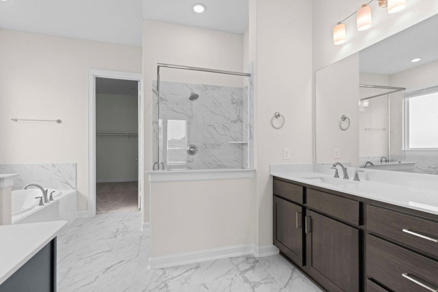 Spa-inspired primary bath featuring dual vanities, granite counters, framed mirrors, and a glass-enclosed shower.