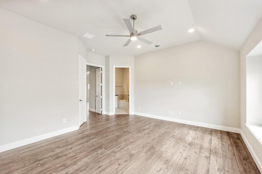 Empty master bedroom with hardwood floors, ceiling fan, and open ensuite bathroom doorway Empty master bedroom with hardwood floors, ceiling fan, and open ensuite bathroom doorway