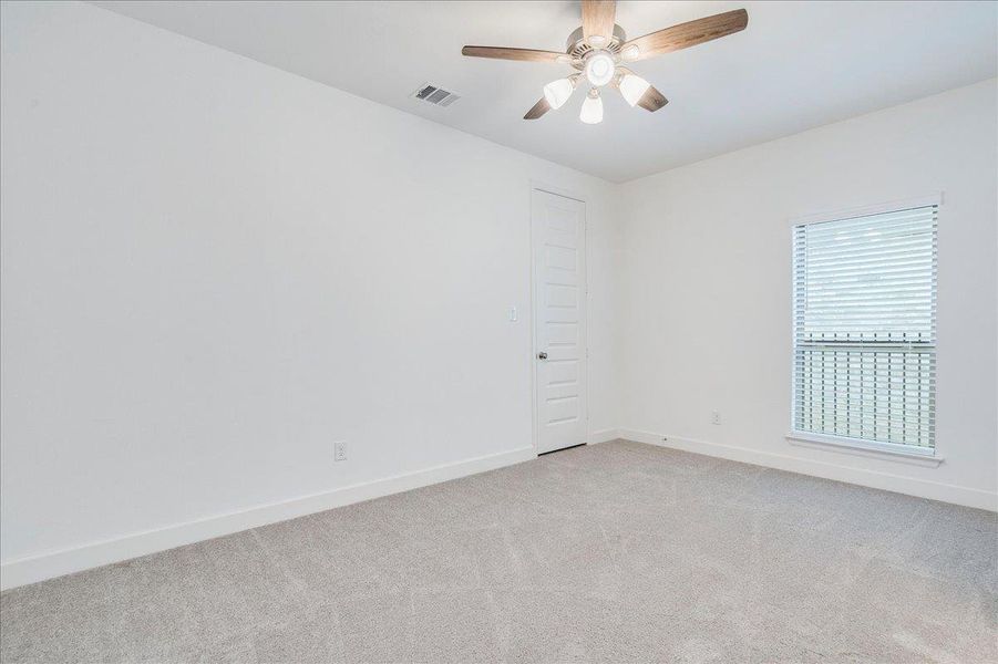 This room features neutral-toned carpet, a ceiling fan with light fixture, and a window with blinds
