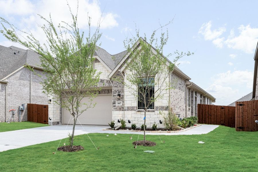 Single-story home with brick and stone exterior, one-car garage, and green front lawn with young trees