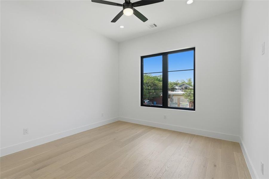 Bright room featuring a large black-framed window, light wood-finish flooring, white walls, a ceiling fan, and recessed lighting Bright room featuring a large black-framed window, light wood-finish flooring, white walls, a ceiling fan, and recessed lighting