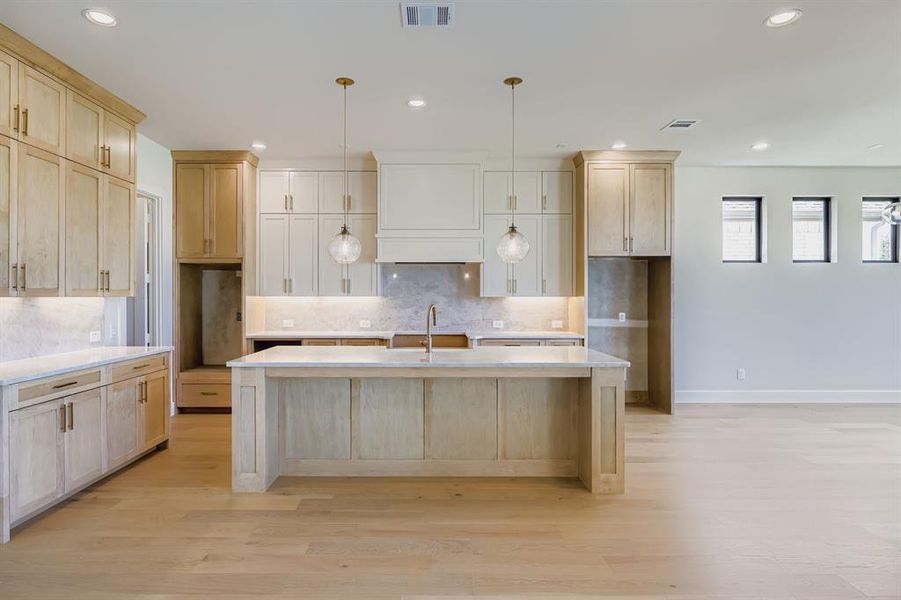 Kitchen with light wood-type flooring, recessed lighting, light countertops, tasteful backsplash, and an island with sink