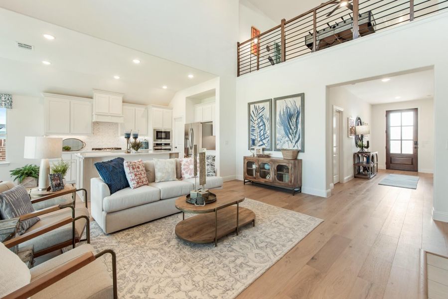 Open-concept living room with two-story ceiling, hardwood floors, and kitchen visible in background Open-concept living room with two-story ceiling, hardwood floors, and kitchen visible in background