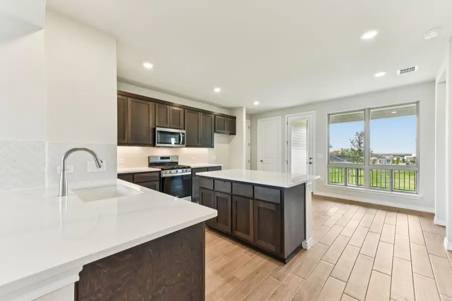 Kitchen with stainless steel appliances, dark brown cabinetry, light stone countertops, a center island, and decorative backsplash