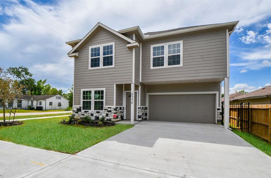 This is a modern two-story corner home with a neutral color palette, featuring a two-car garage, a well-maintained lawn, and a stone accent around the front entrance.