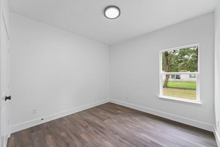 Bright room with wood-finish flooring, white walls, and a single window offering exterior views Bright room with wood-finish flooring, white walls, and a single window offering exterior views