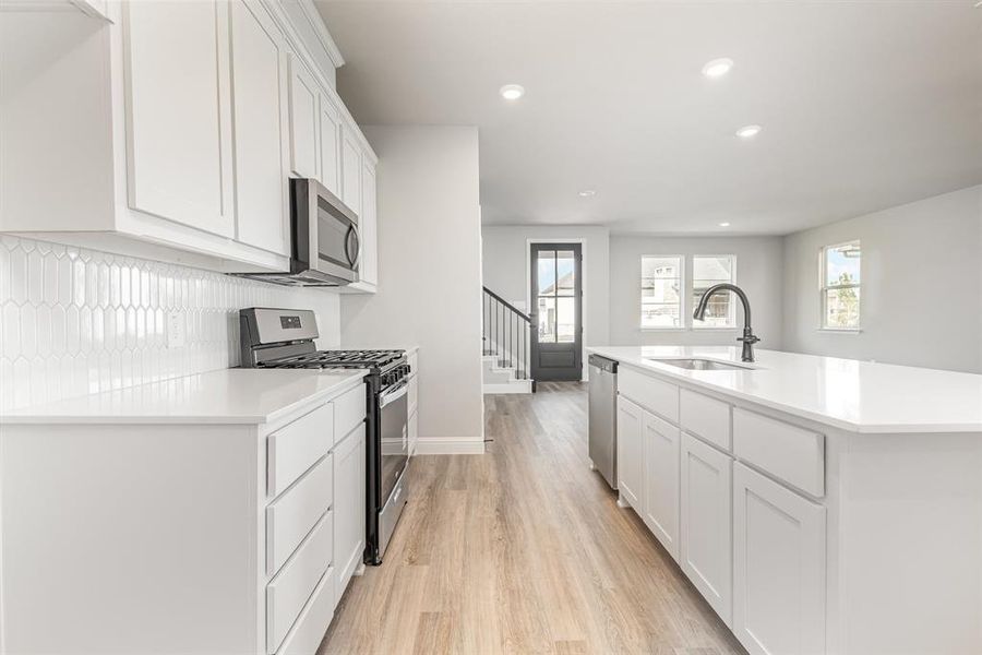 Kitchen with appliances with stainless steel finishes, white cabinets, light wood finished floors, recessed lighting, and an island with sink