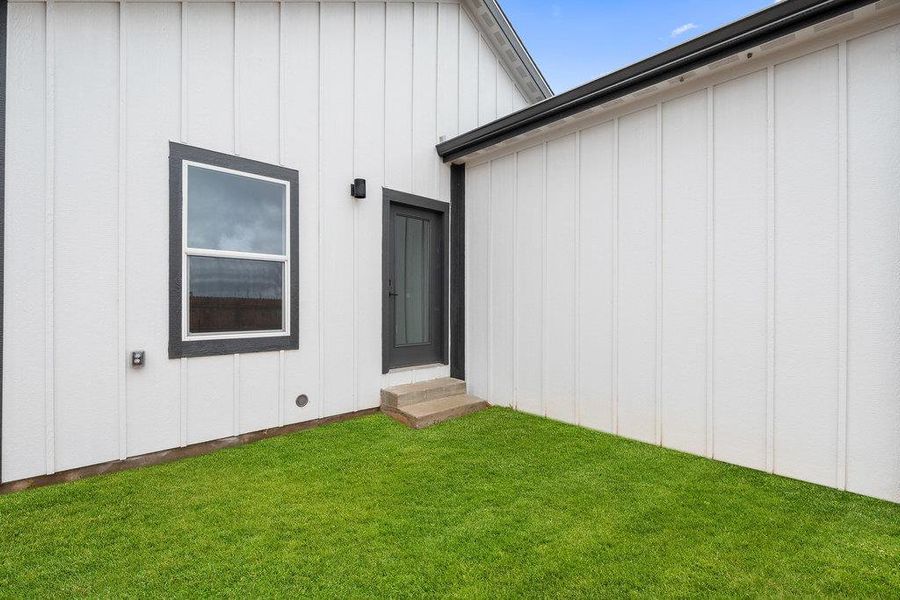 Entrance to property featuring board and batten siding and a lawn