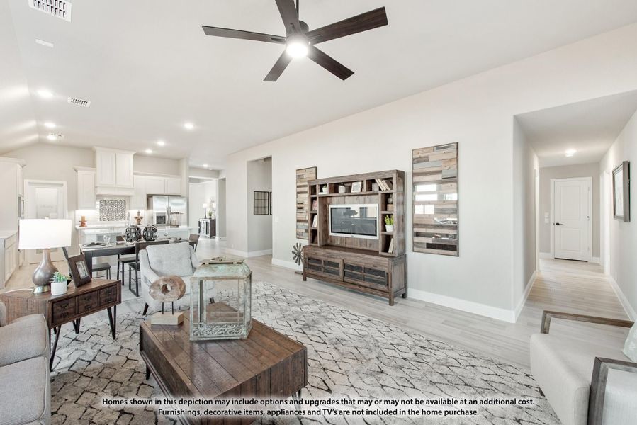 Open-concept living room with ceiling fan, wood entertainment center, and light hardwood floors, open to kitchen and dining area.