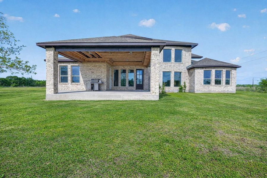 Rear exterior property 1 unfinished residence,  with covered patio, open backyard, and virtually enhanced lawn.