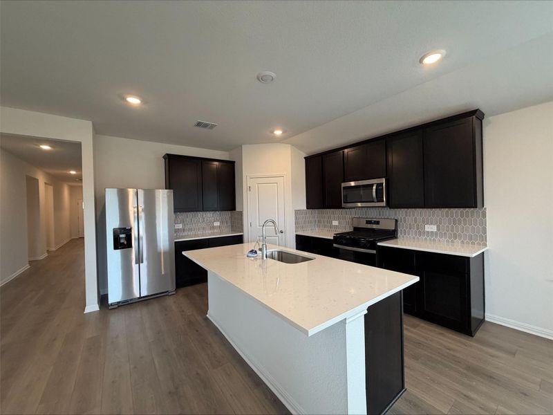 Kitchen featuring stainless steel appliances, tasteful backsplash, light stone countertops, dark wood-style floors, and recessed lighting