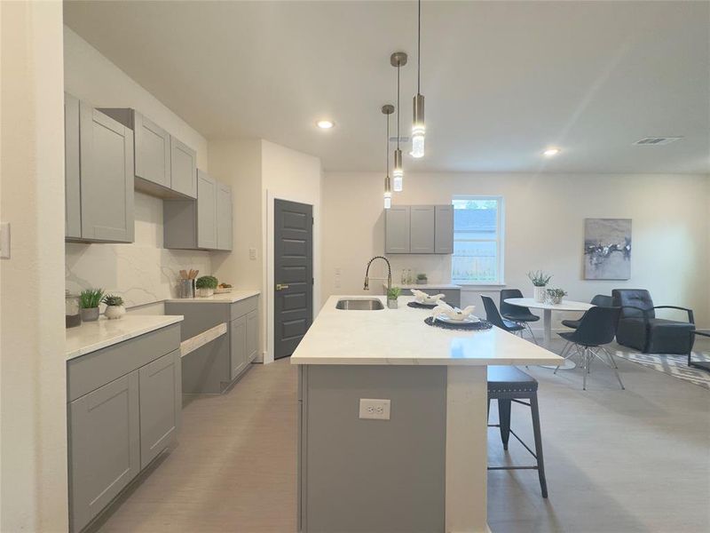 Kitchen with a kitchen island with sink, gray cabinets, sink, and hanging light fixtures