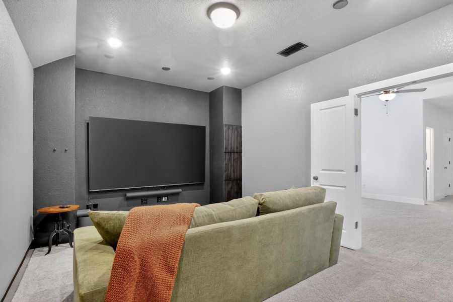 Media room featuring a large mounted screen, dark accent wall, recessed lighting, and light gray wall-to-wall carpeting Media room featuring a large mounted screen, dark accent wall, recessed lighting, and light gray wall-to-wall carpeting