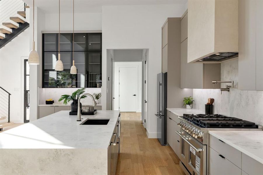 Gourmet kitchen featuring a substantial island with integrated sink, sleek pot filler faucet, professional-grade range, stainless steel French-door refrigerator, and floor-to-ceiling cabinetry with grid glass accents