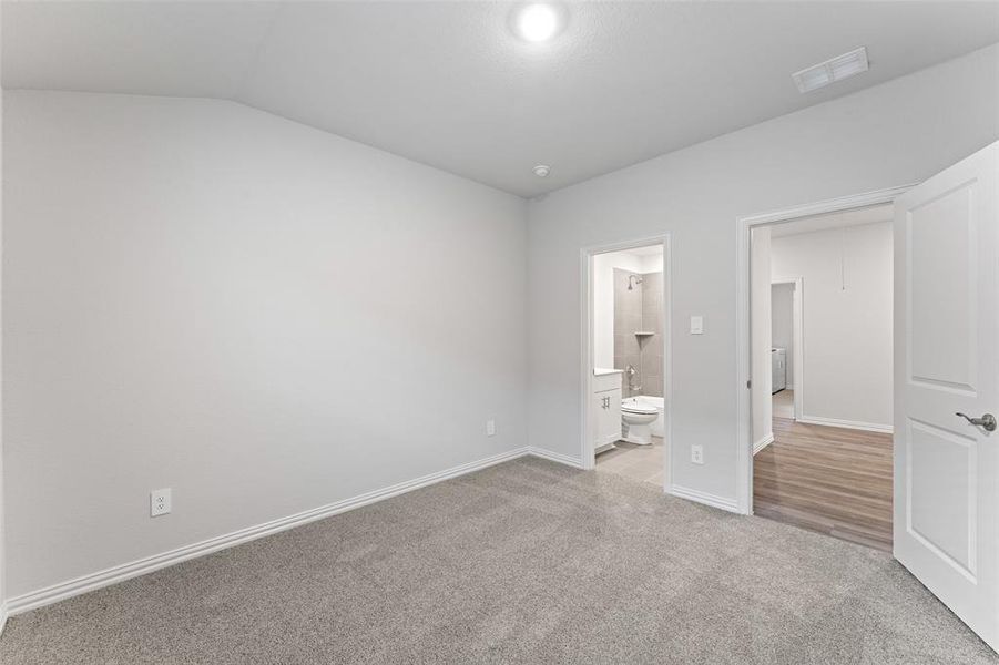 Unfurnished bedroom with carpet flooring, vaulted ceiling, and ensuite bath Unfurnished bedroom with carpet flooring, vaulted ceiling, and ensuite bath