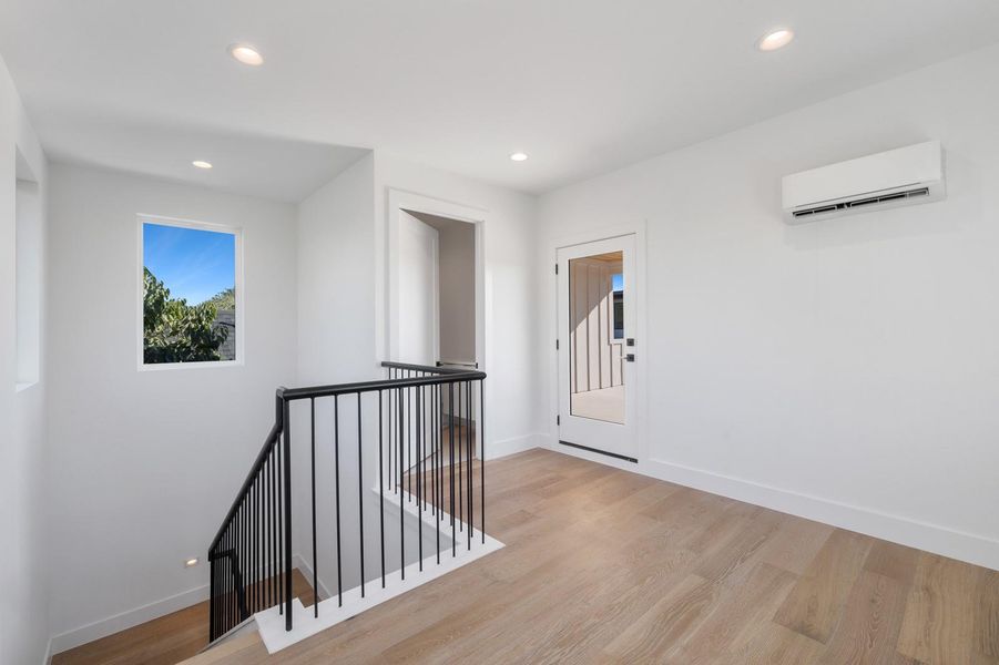 Hallway with an upstairs landing, recessed lighting, light wood-type flooring, and a wall mounted air conditioner