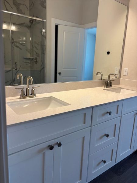Bathroom featuring a marble finish shower, double vanity, and dark wood-style floors