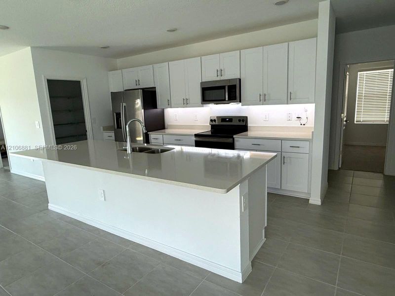 Kitchen featuring white shaker-style cabinetry, a large island with a composite countertop, under-cabinet lighting, stainless steel appliances, and tile flooring