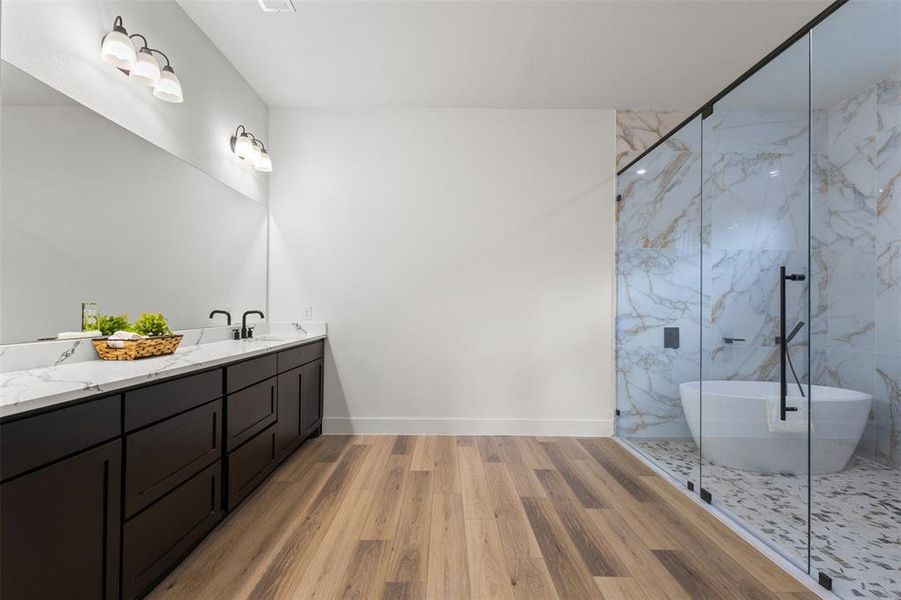 Bathroom with double vanity, light wood-style flooring, a soaking tub, and a marble finish shower