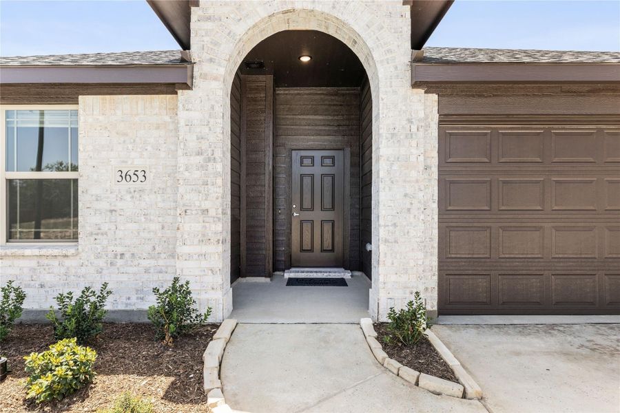 Home entrance with arched brick surround, dark wood front door, and two-car garage at address 3653