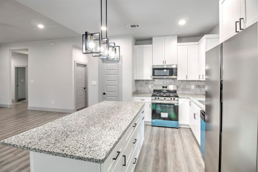 Kitchen featuring stainless steel appliances, pendant lighting, backsplash, light wood-style floors, and recessed lighting Kitchen featuring stainless steel appliances, pendant lighting, backsplash, light wood-style floors, and recessed lighting