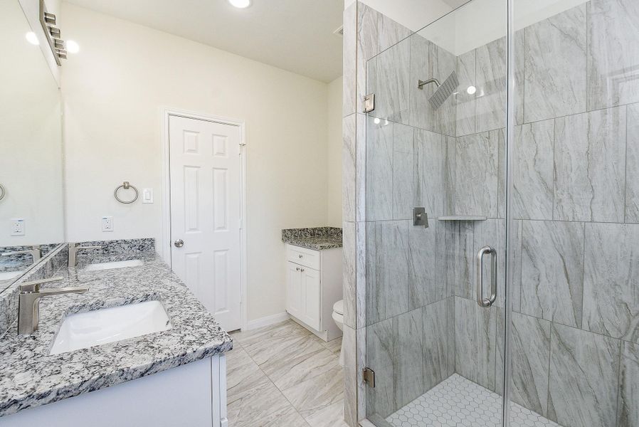 Modern bathroom with marble tiles, glass shower, white vanity with granite countertop, and large mirror. Clean and bright interior.