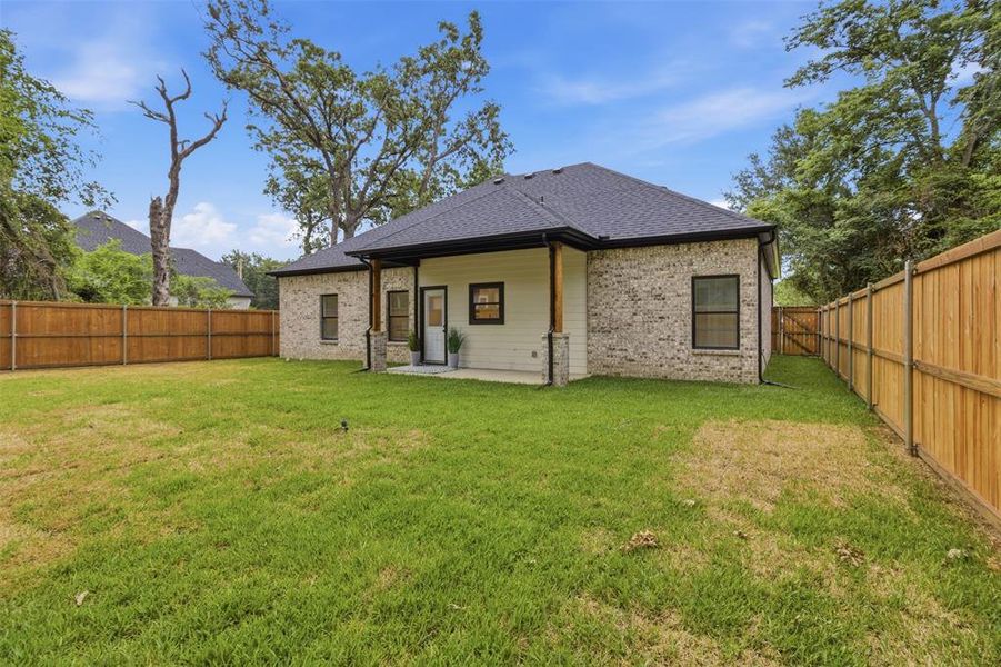 Spacious backyard featuring a wood privacy fence, a covered patio with wood columns, and a light brick and siding exterior