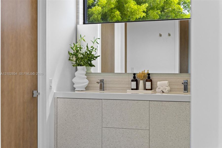 Floating vanity with textured cabinetry, solid surface countertop, linear tile backsplash, horizontal mirror, and chrome dual-faucet fixtures